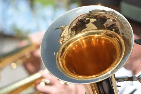Glänzender Schallbecher einer kleinen Tuba, der eine belebte Straße mit Menschen und Gebäuden widerspiegelt.