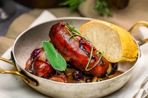 Herzhafte, selbstgemachte Salsiccia mit Rotkohl und Brot in einer Pfanne, garniert mit Salbei und Rosmarin.