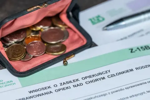 Portmonetka z monetami obok wniosku o zasiłek opiekuńczy. Dokumenty i drobne pieniądze symbolizują wsparcie finansowe dla opiekunów.