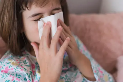 Dziewczynka z katarem wyciera nos chusteczką. Może potrzebuje antybiotyku na zatoki.