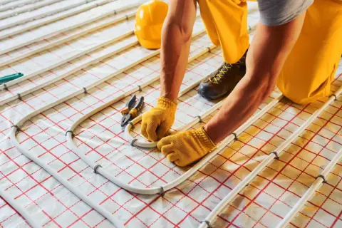 Instalator montuje rury do suchego ogrzewania podłogowego. Wady tego systemu mogą obejmować nierównomierne grzanie.