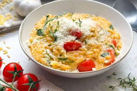Schüssel mit Orzotto, Tomaten, Spinat und Parmesan, garniert mit Thymian.