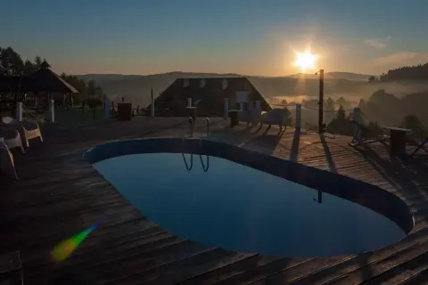 Poranek nad basenem z widokiem na Bieszczady. Słońce wschodzi nad mglistymi dolinami, tworząc magiczną atmosferę. Idealne miejsce na relaks w **termy Bieszczady**.