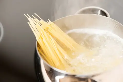 Kluska spaghetti zanurza się w gotującej wodzie. Czy wode na makaron sie soli? Tak, aby nadać jej smak.