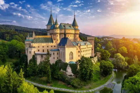 Bajkowy zamek otoczony zielenią, idealne miejsce na nocleg w zamku. Słońce zachodzi nad wzgórzami, tworząc magiczną atmosferę.