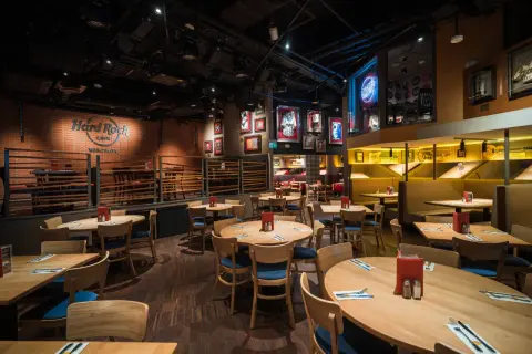 Wnętrze Hard Rock Cafe Warszawa. Drewniane stoły i krzesła, ściany ozdobione pamiątkami muzycznymi i neonem "Rock Radio".
