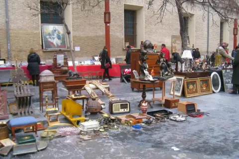Mercadillo en la plaza San Bruno con antigüedades, muebles y objetos decorativos expuestos en el suelo y mesas.