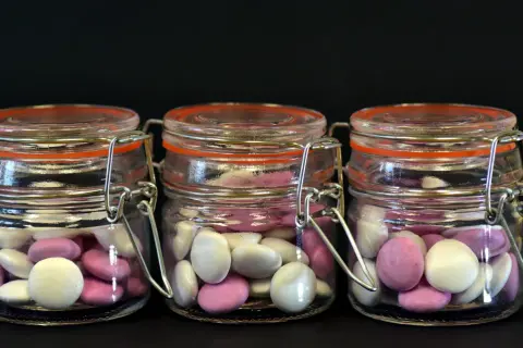Trois bocaux en verre remplis de bonbons roses et blancs, une idée originale par quoi remplacer les dragées mariage.