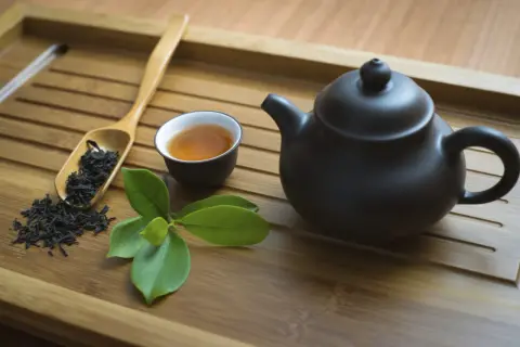 Service à thé en bambou avec théière noire, tasse de thé ambré, feuilles de thé et une branche de feuilles vertes. Parfait pour un thé sans théine.