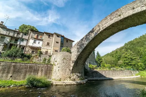 Antico ponte in pietra a schiena d'asino, con case aggrappate alla collina. Un scorcio suggestivo del portico di Romagna.