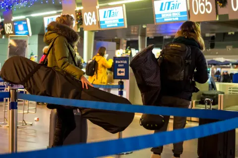 Osoby z bagażem sportowym, w tym futerałem na instrument, czekają na odprawę na lotnisku. Idealny bagaż sportowy Ryanair na podróż.