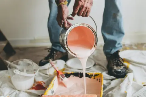 Mani versano pittura murale a spruzzo in una vaschetta per rulli. Preparazione per un nuovo colore.