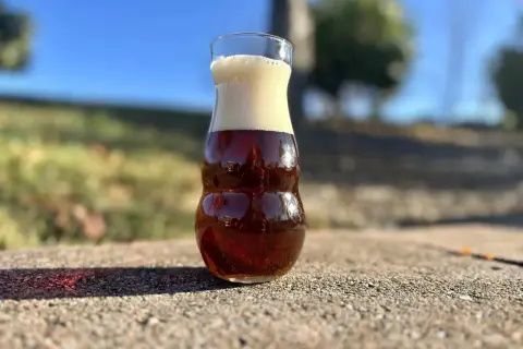 Szklanka z pianką, w środku bursztynowe piwo amber ale, odbijające domki.