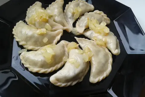 Pyszne pierogi z płuckami, polane skarmelizowaną cebulką, kuszą na czarnym talerzu.