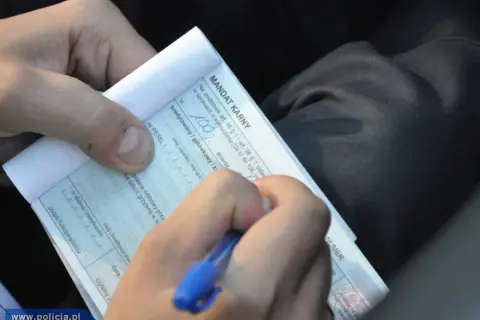 Ręka pisze mandat karny. Zastanawiasz się, ile czasu na zapłacenie mandatu? Dokument zawiera informacje o kwocie i terminie.