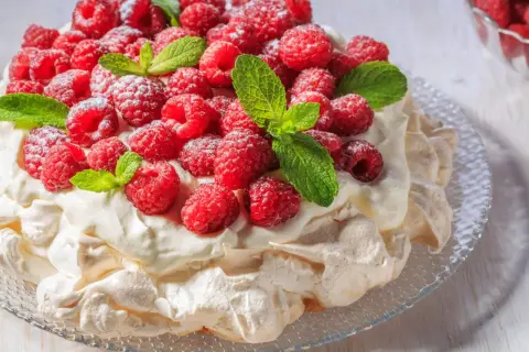 Beza Pavlova, która zawsze wychodzi, udekorowana świeżymi malinami i listkami mięty, posypana cukrem pudrem.