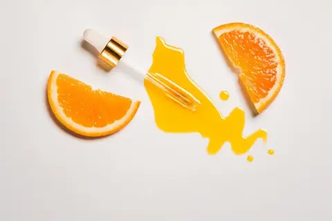 Ein Pipettenfläschchen tropft ein leuchtendes Serum neben Orangenscheiben. Vitamin C für das Gesicht, das für strahlende Haut sorgt.