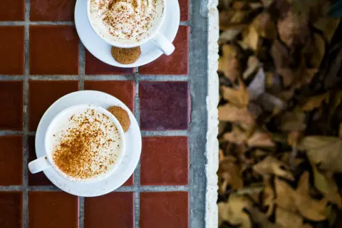 Två koppar med krämig pumpkin spice latte, toppade med kanel och en pepparkaka. Perfekt för ett mysigt pumpkin spice latte recept.