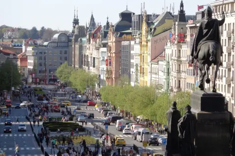 Pomnik konny na placu Wacława w Pradze, z widokiem na tętniącą życiem ulicę pełną ludzi i samochodów.