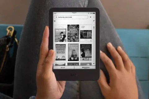 Une personne tient un Kindle affichant des livres, une invitation à découvrir un livre Kindle gratuit.
