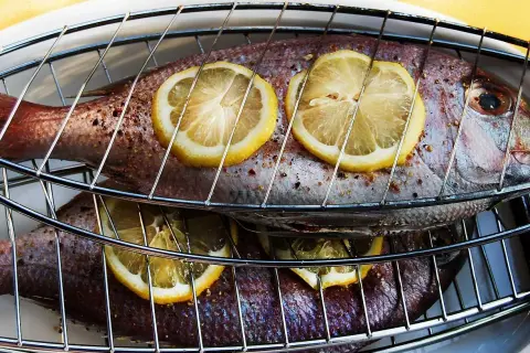 Två hela fiskar ligger på ett grillgaller, toppade med citronskivor. Snart är det dags att grilla fisk!