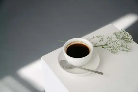 En vit kaffekopp med en sked och en liten blomsterkvist. Kanske inte det bästa valet om man är dålig i magen av kaffe på morgonen.