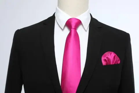 Un completo nero con camicia bianca, una cravatta rosa acceso e un fazzoletto da taschino coordinato. Un abbinamento audace e di classe.