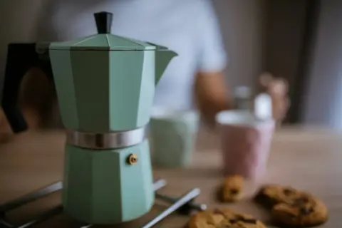 Moka verde pronta per il caffè, ma forse manca qualcosa per capire perche la moka non fa il caffe. Biscotti e tazze sullo sfondo.
