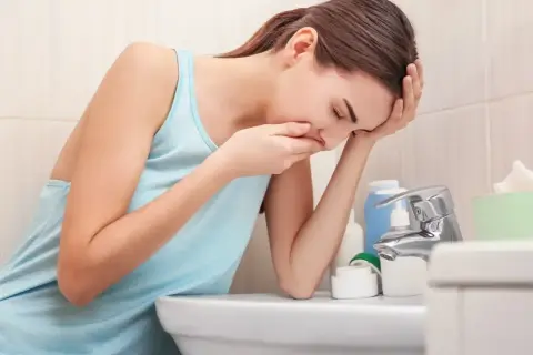 Kobieta w łazience, z ręką na ustach, doświadcza mdłości w ciąży.