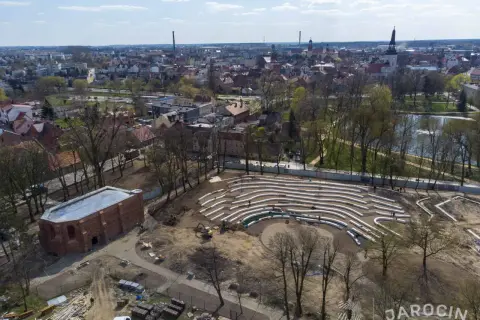 Nowe amfiteatralne trybuny w jarocińskim parku nabierają kształtów. W tle widać panoramę miasta i staw.