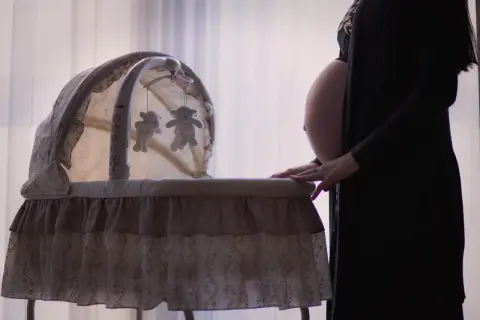 Gravid kvinna med ruckbart huvud vid en vagga med nallar.