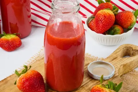Frische Erdbeeren werden zu einem leckeren Smoothie verarbeitet. Eine Flasche mit dem roten Fruchtgetränk steht bereit.