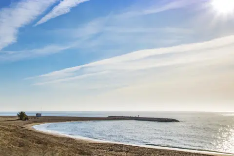 Playa de Macenas en Almería, con un muelle y el sol brillando en el mar.
