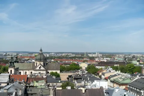 Widok na krakowskie dachy i kościół z kopułą. W tle nowoczesne budynki, które mogą wpływać na ceny mieszkań w Krakowie za m2.