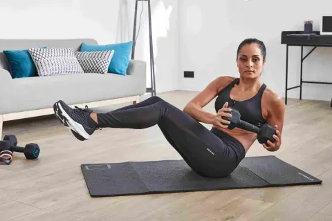 Femme faisant des torsions russes avec haltère, un exercice de gym facile pour débutant, dans un salon moderne.