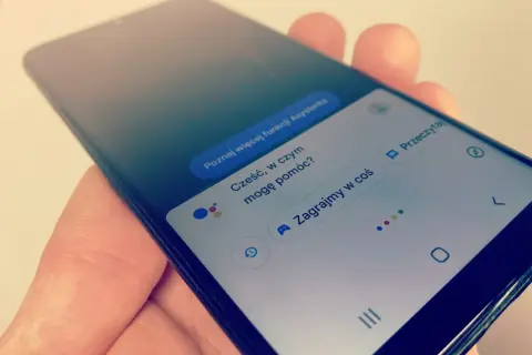 Smartfon z Asystentem Google, który czeka na **wyszukiwanie głosowe**. Widoczne opcje: "Poznaj więcej funkcji Asystenta", "Cześć, w czym mogę pomóc?", "Zagrajmy w coś".