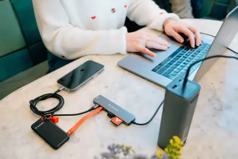 Kobieta pracuje na laptopie, podłączając telefon, dysk zewnętrzny i kartę SD do huba USB 3.2 Gen. 1.
