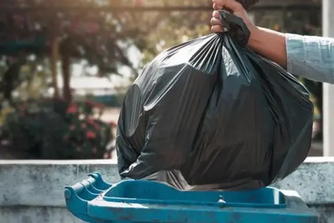 Mano depositando bolsa de basura en contenedor azul. ¿Quién paga la tasa de basura en un alquiler?