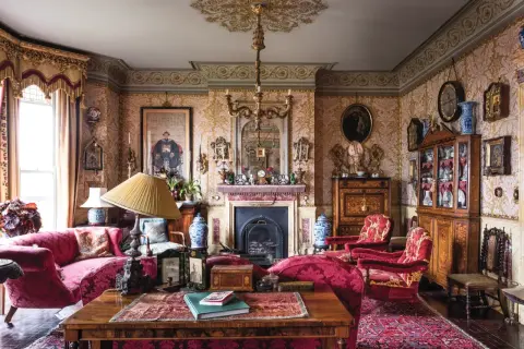 A lavish Victorian interior design with ornate wallpaper, plush red furniture, a fireplace, and antique decor.