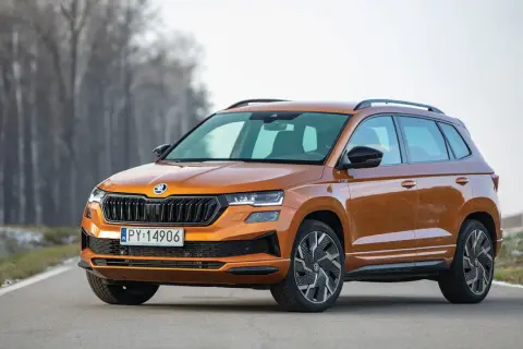Pomarańczowy Skoda Karoq Sportline na drodze, z drzewami w tle.