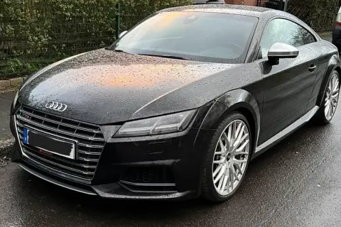 Negro Audi TT RS mojado por la lluvia, con reflejos naranjas en el capó. El coche está listo para la etapa 1 de su viaje.