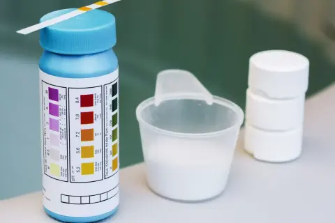 Teststreifen für den ph-wert pool, daneben ein Messbecher mit weißem Pulver und Tabletten.