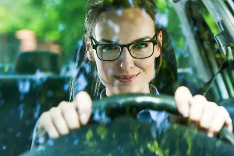 Frau mit Brille am Steuer, bereit zum Autofahren.