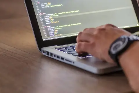 Dłoń programisty pisze kod na laptopie. Zastanawiasz się, ile zarabia programista po studiach?