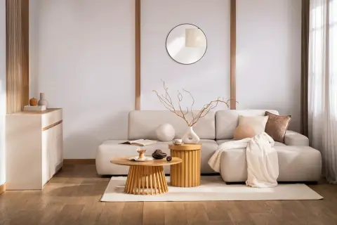Salon w stylu zen. Jasna kanapa, drewniane stoliki, okrągłe lustro i subtelne dekoracje tworzą oazę spokoju.