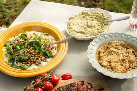Tre skålar med röror, en med yoghurt och nötter, en grön och en orange, perfekt gott till grillat.
