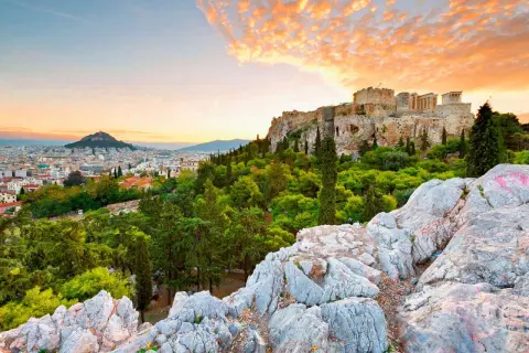 Akropolis reser sig över Aten, greklands huvudstad, med en dramatisk solnedgång i bakgrunden.