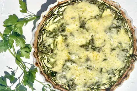Eine köstliche Zucchini-Quiche mit goldbraunem Teig und einer cremigen Füllung, garniert mit frischer Petersilie.