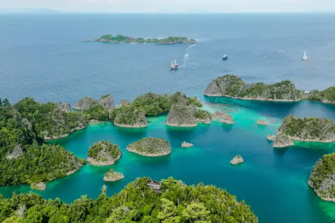 Traumhafte Anreise nach Raja Ampat: türkisfarbene Lagunen, grüne Inseln und Segelschiffe im azurblauen Meer.
