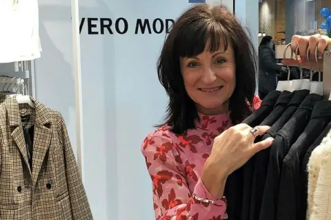 En glad kvinna i en blommig blus vid en klädställning med kläder från en Vero Moda återförsäljare.